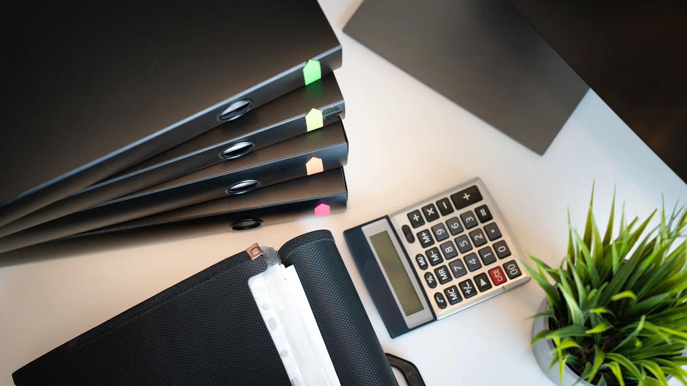 Stacked ring binders, a calculator and a potted plant on a desk, organized audit and compliance documentation