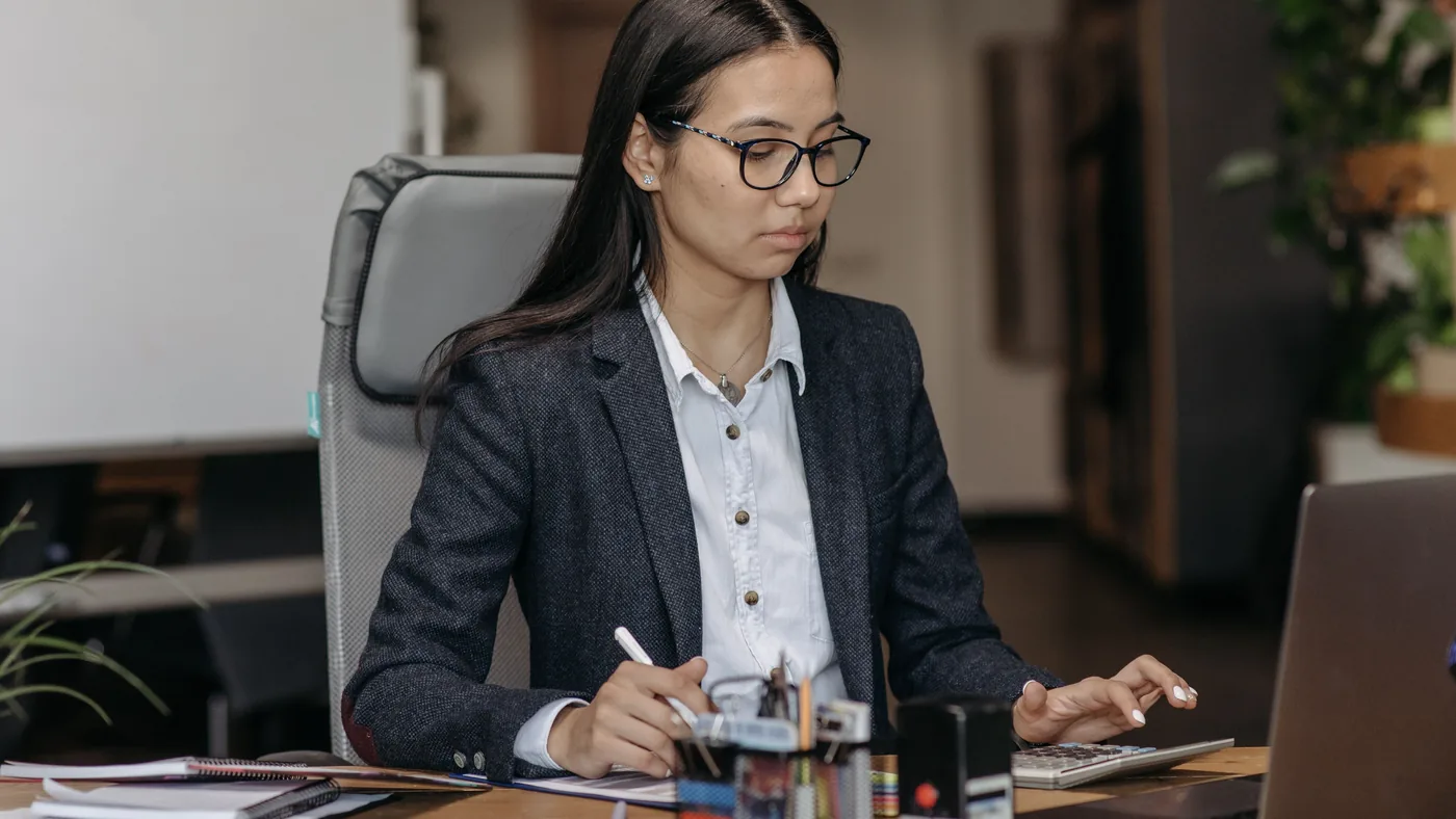 A professional working at a desk with a laptop and calculator in an office